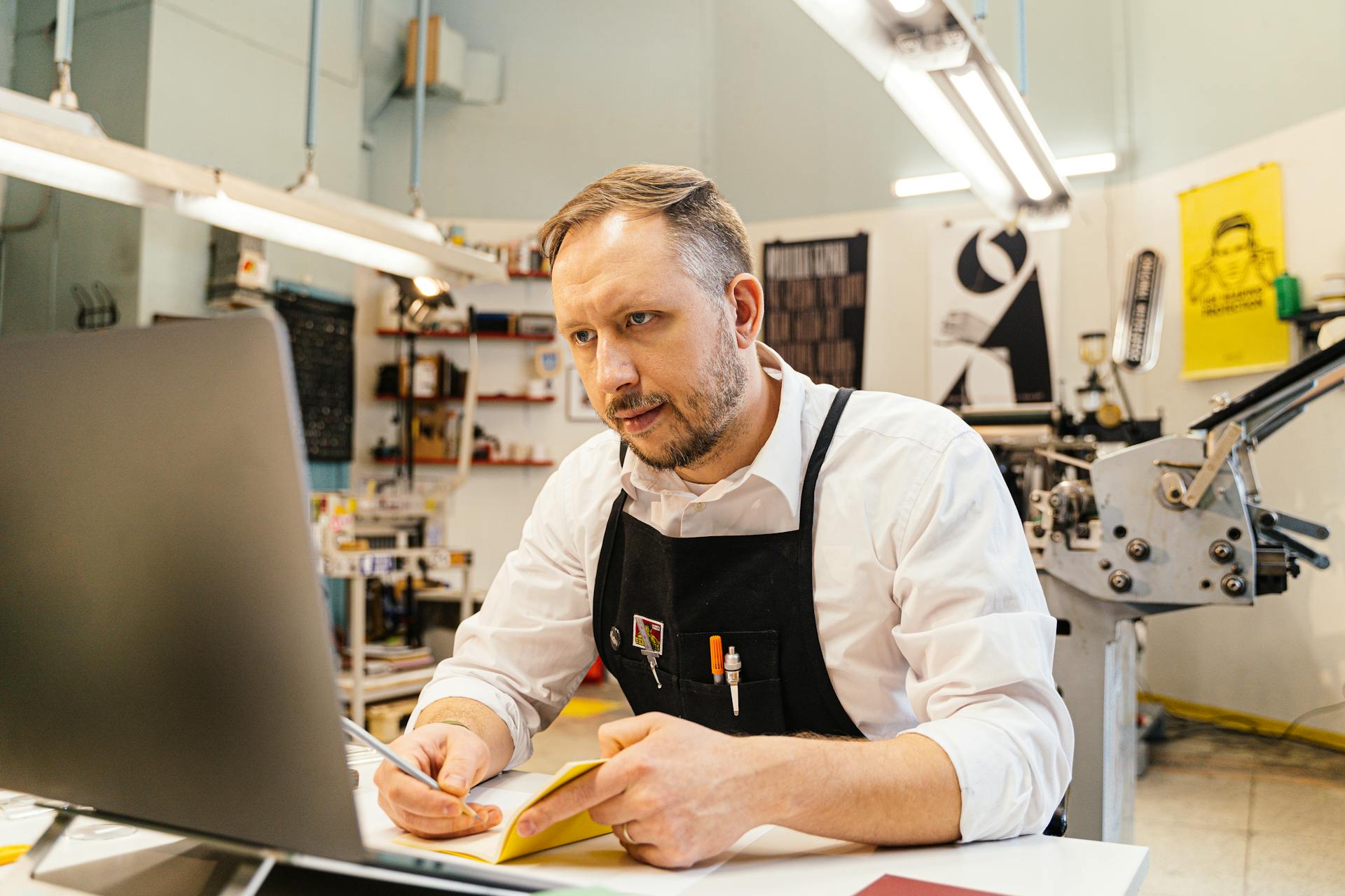 A dedicated man working at his computer within a busy print shop space, focusing intently.