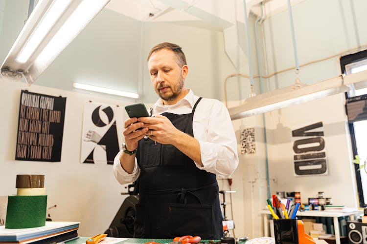 Graphic Designer In A Studio With Posters Using Phone