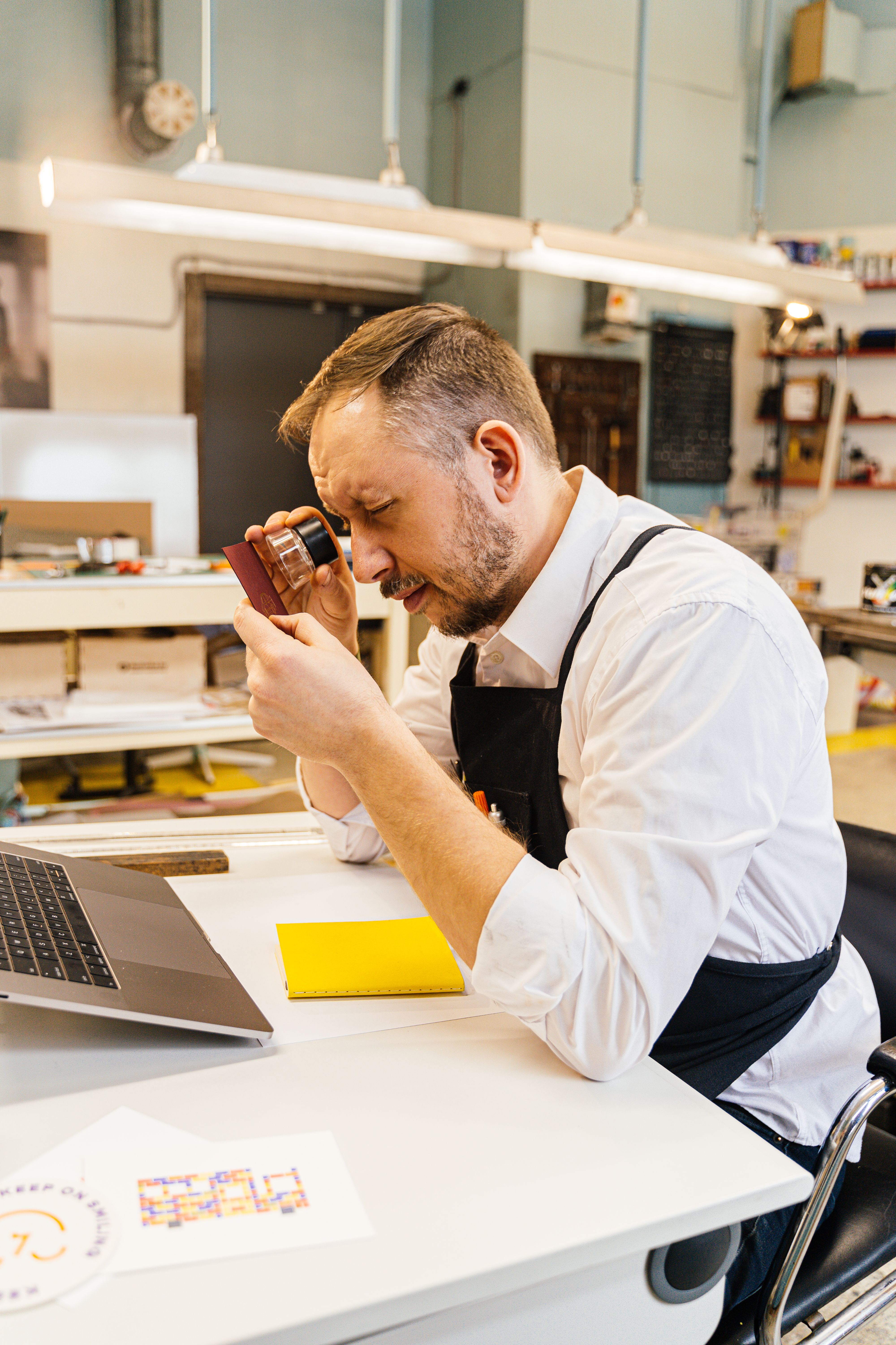 Focused man using a magnifier in a creative office space, examining details for a printing project.