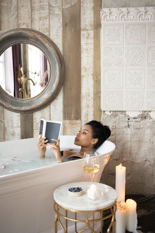 Free Young black woman reading book in bath Stock Photo