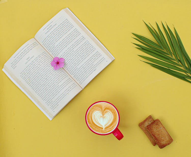 Top View Of An Open Book And A Mug Of Coffee On Yellow Background