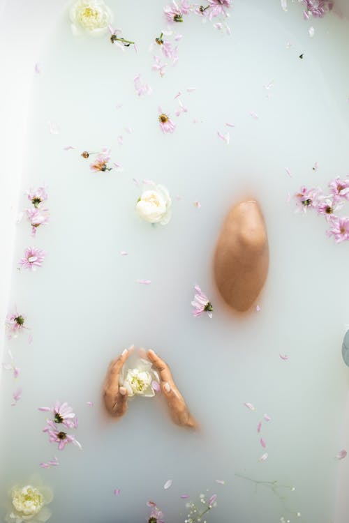 Faceless lady in milk bath with flower petals