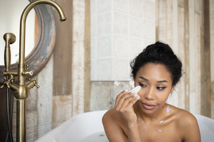 Black Woman Doing Facial Massage In Bathtub With Metal Faucet