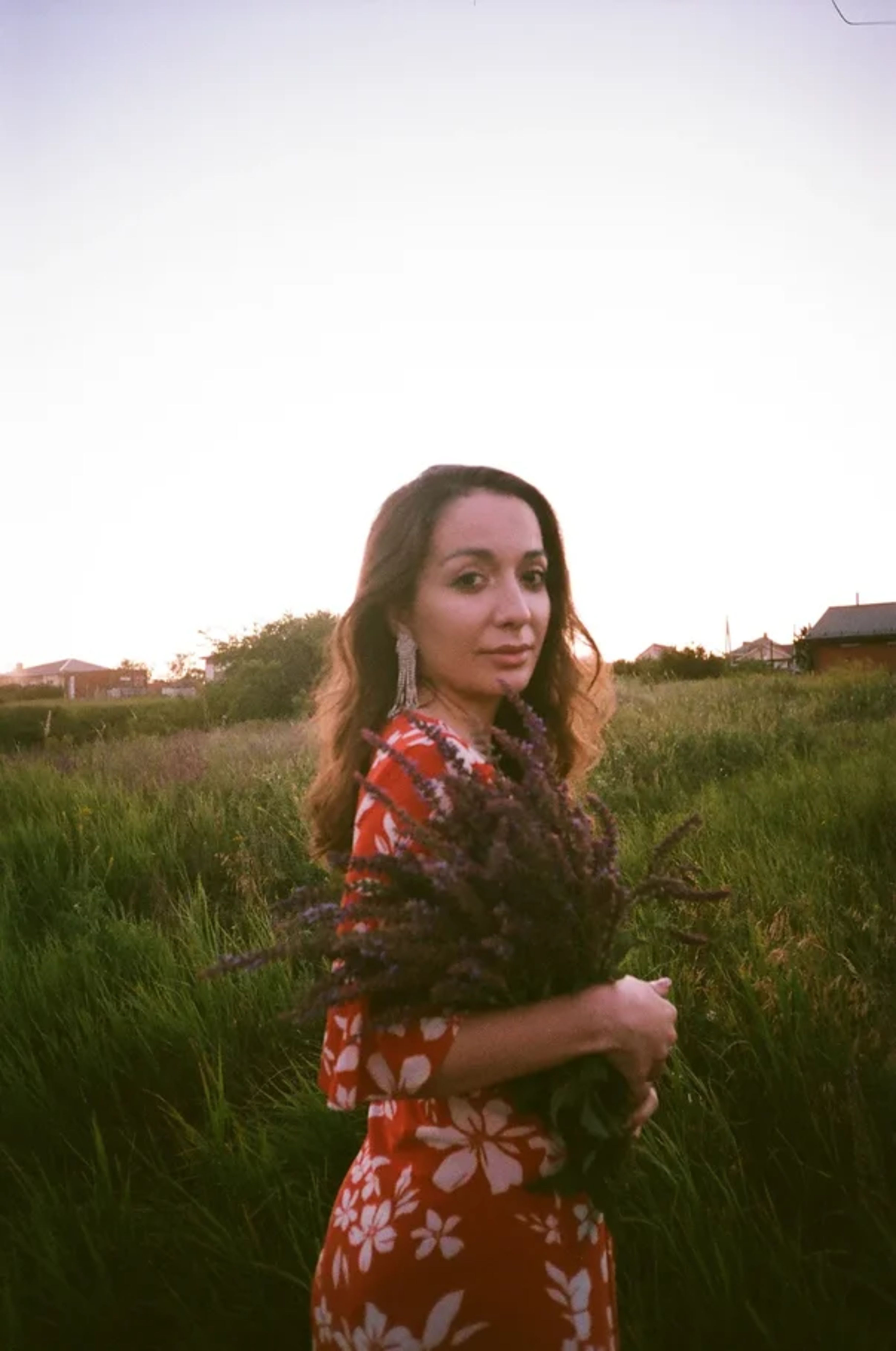 A woman in a floral dress stands in a field holding lavender during sunset in Rostov-on-Don, Russia.