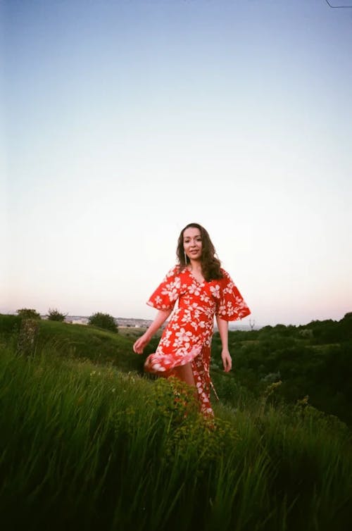 Woman in a White and Red Floral Dress Walking on a Grass Field