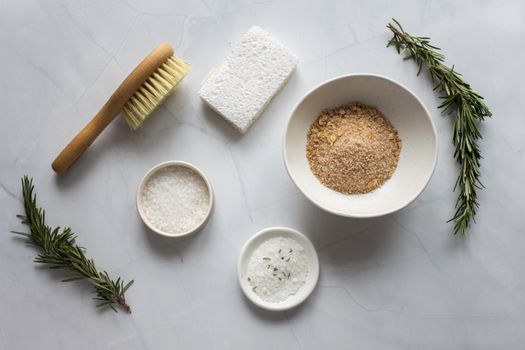 Top view of bowls with ingredients for organic scrub arranged with pumice stone and fresh branches of rosemary