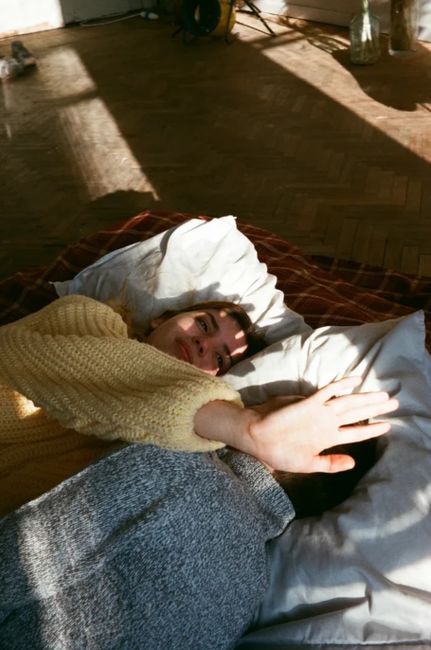 A woman in a cozy sweater enjoying a calm morning indoors, lying on pillows.