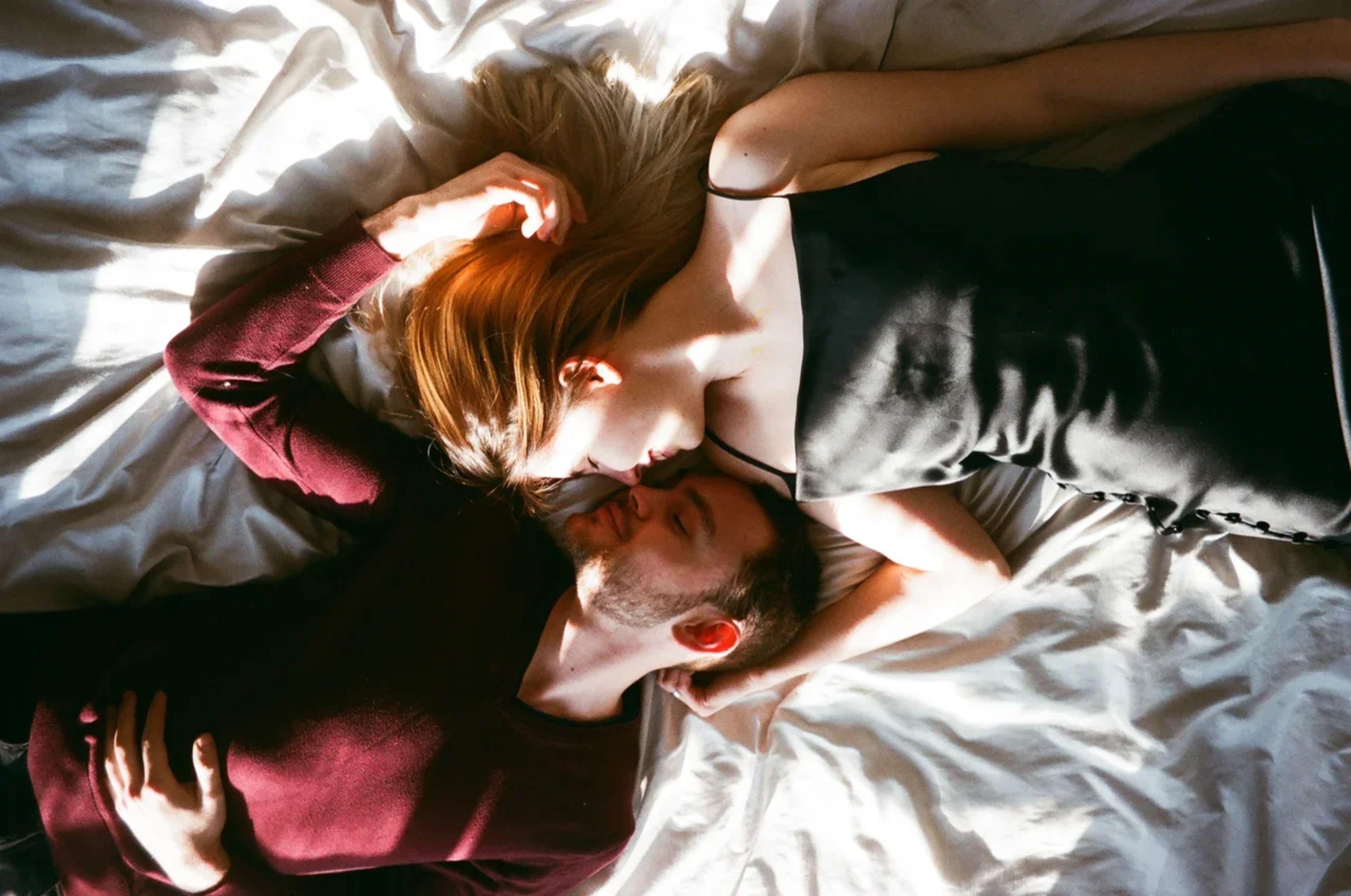 A tender moment captured from above, showing a couple in an intimate embrace on a bed, bathed in sunlight.