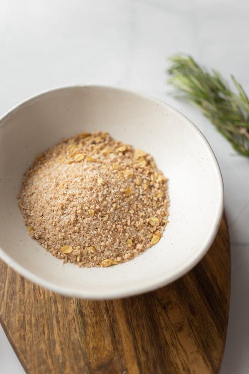 Free From above of plate filled with milled oat flakes on wooden board near branch of rosemary Stock Photo