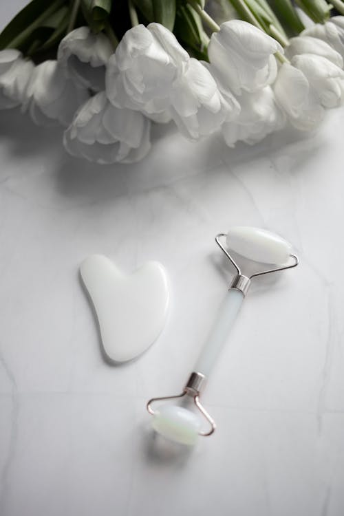 From above of Gua sha massage tools placed near fresh bouquet of white tulips on marble table in daylight