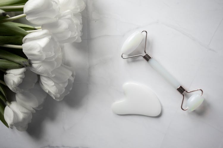 White Gua Sha Tools Placed Near Bouquet Of Flowers On Marble Table