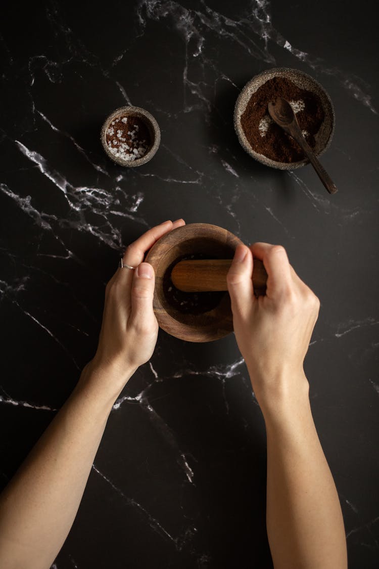 Female Mixing Coffee And Salt In Mortar On Black Marble Table