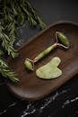 From above of Jade roller and Gua Sha massage tool placed on wooden plate on black marble table with fresh twigs of rosemary