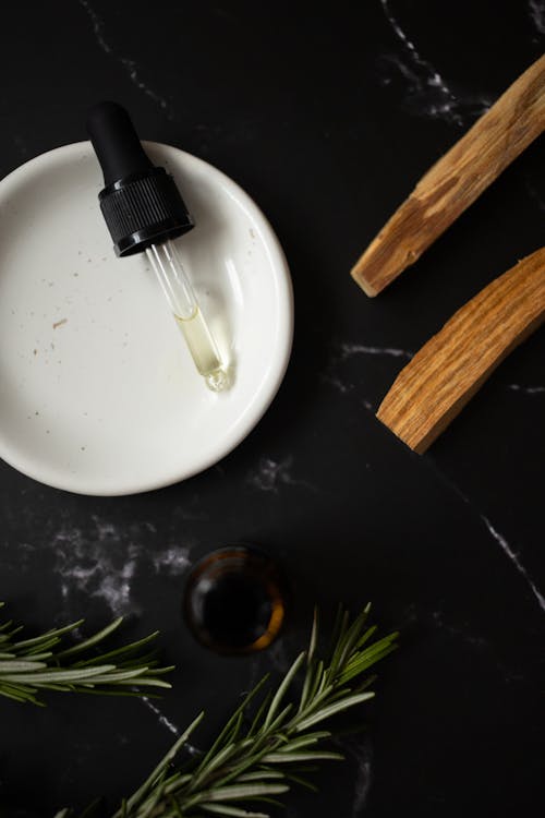 Top view of white clean plate with aromatic oil composed with timber sticks and fresh verdant branches of rosemary