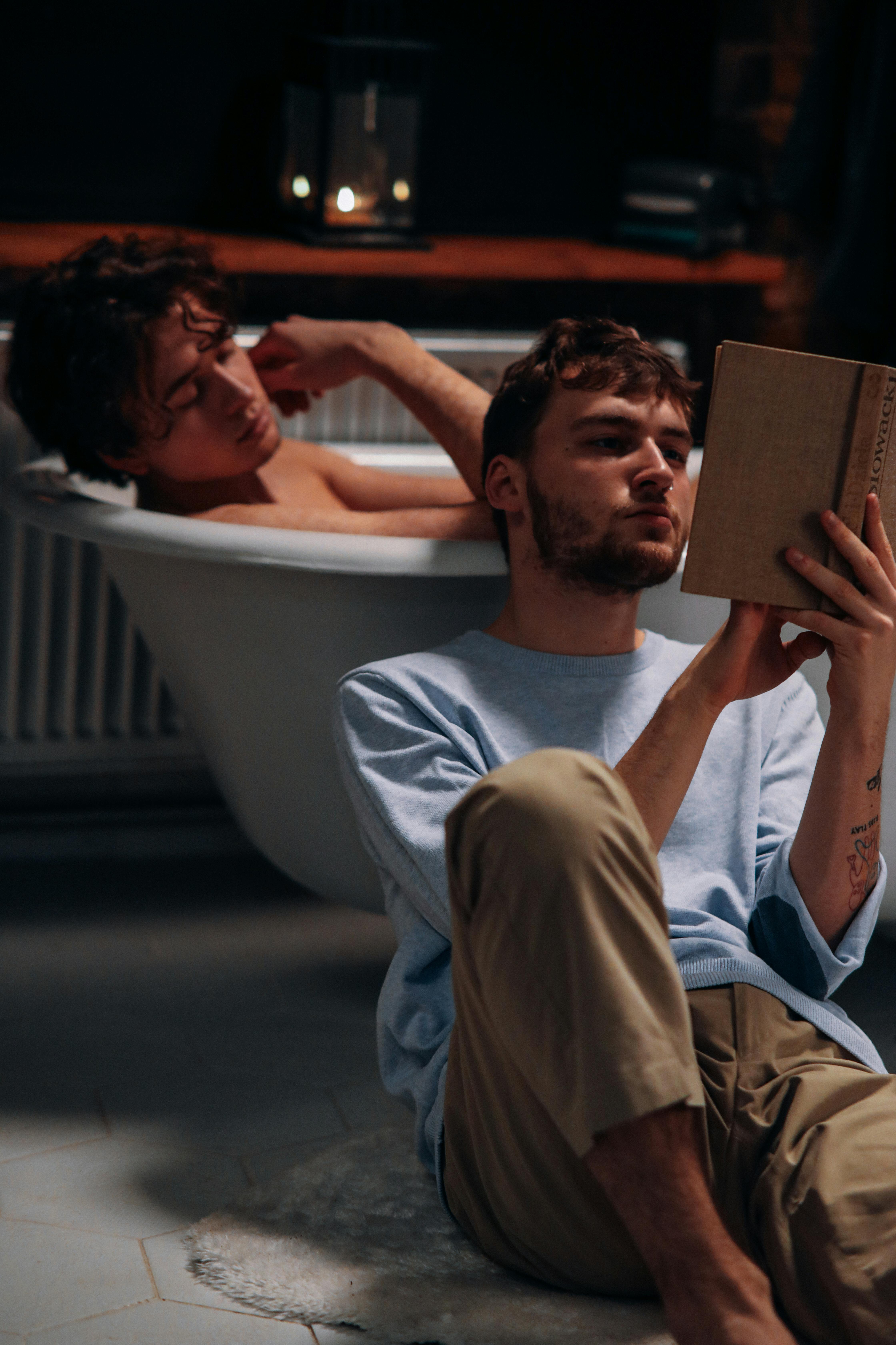 photo of a man taking a bath near a man reading a book