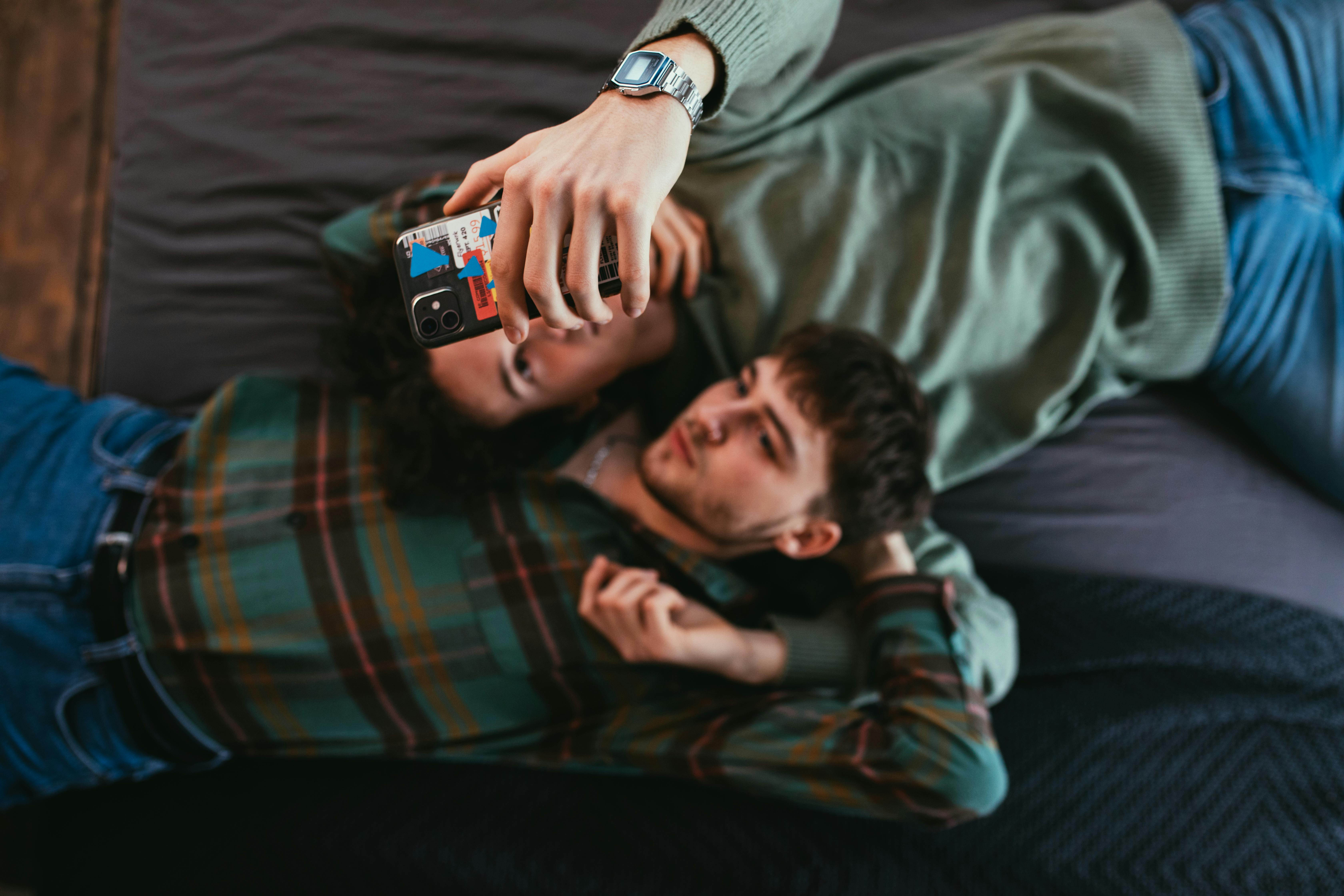 men lying on bed while looking at the screen of a cellphone
