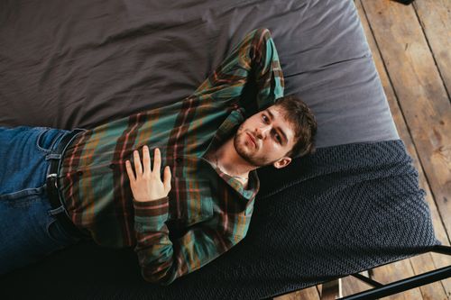 Free Man in plaid shirt relaxing on a bed in a cozy bedroom setting. Stock Photo