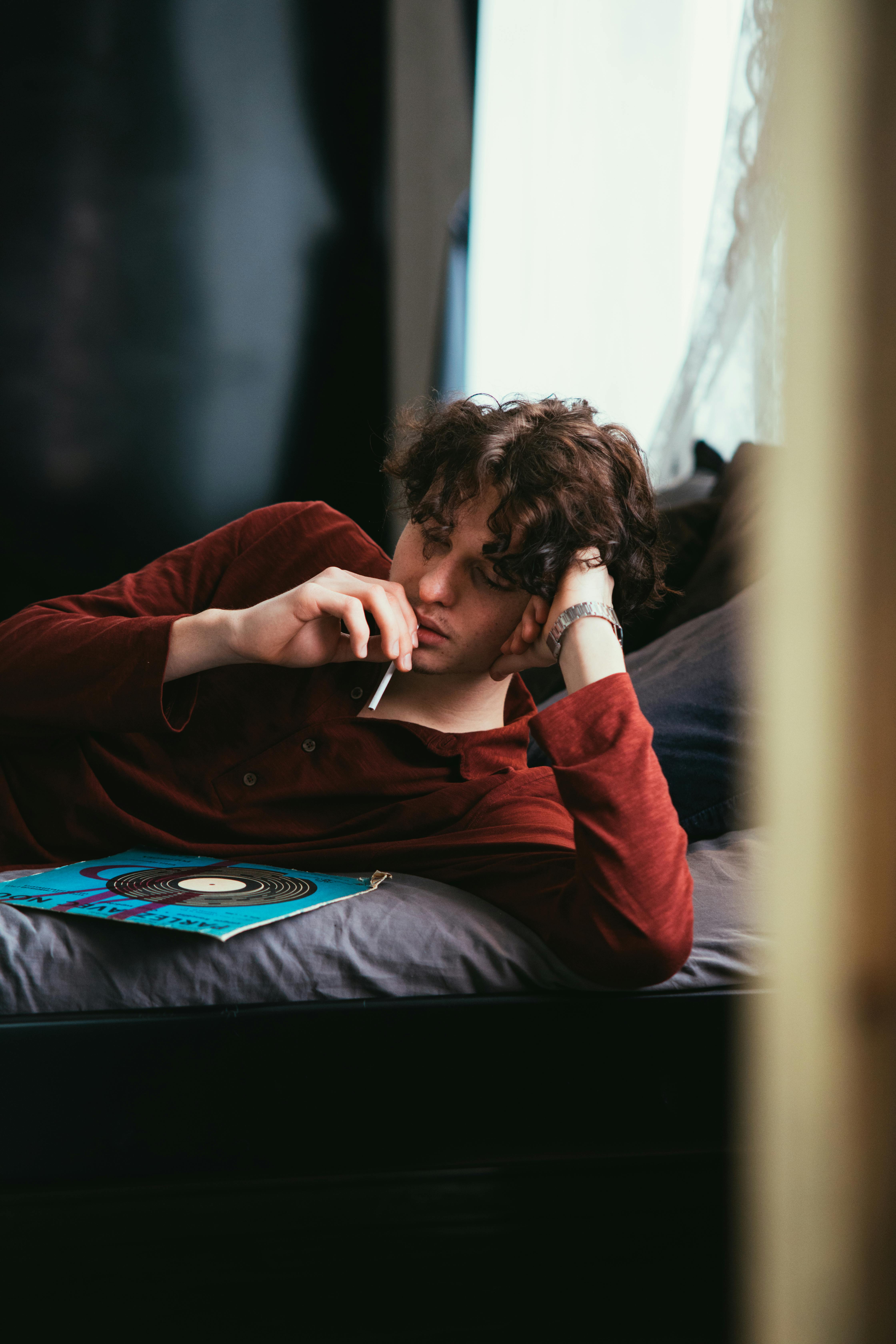 man in red shirt lying on sofa looking at vinyl record