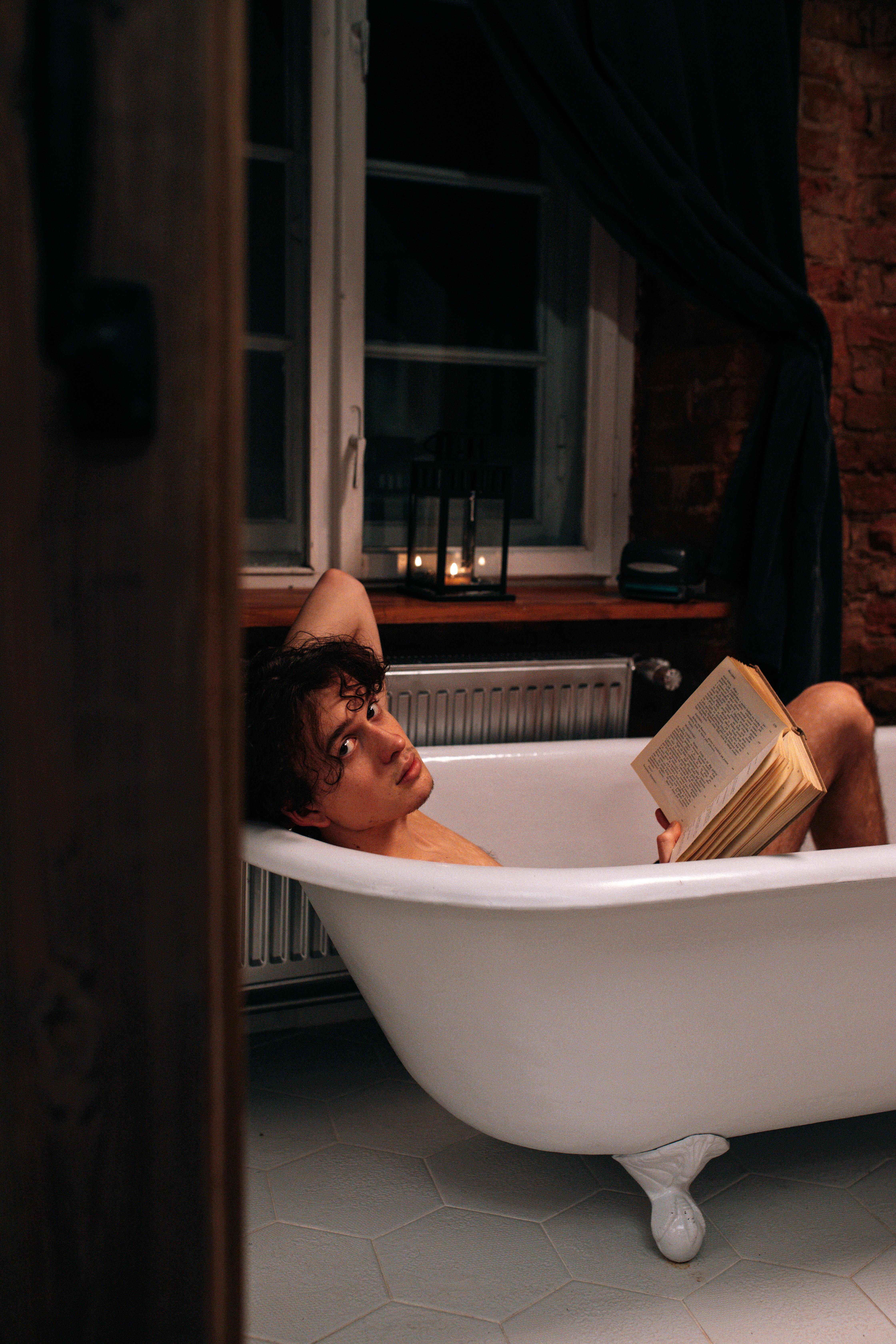 photo of a topless man taking a bath while holding a book