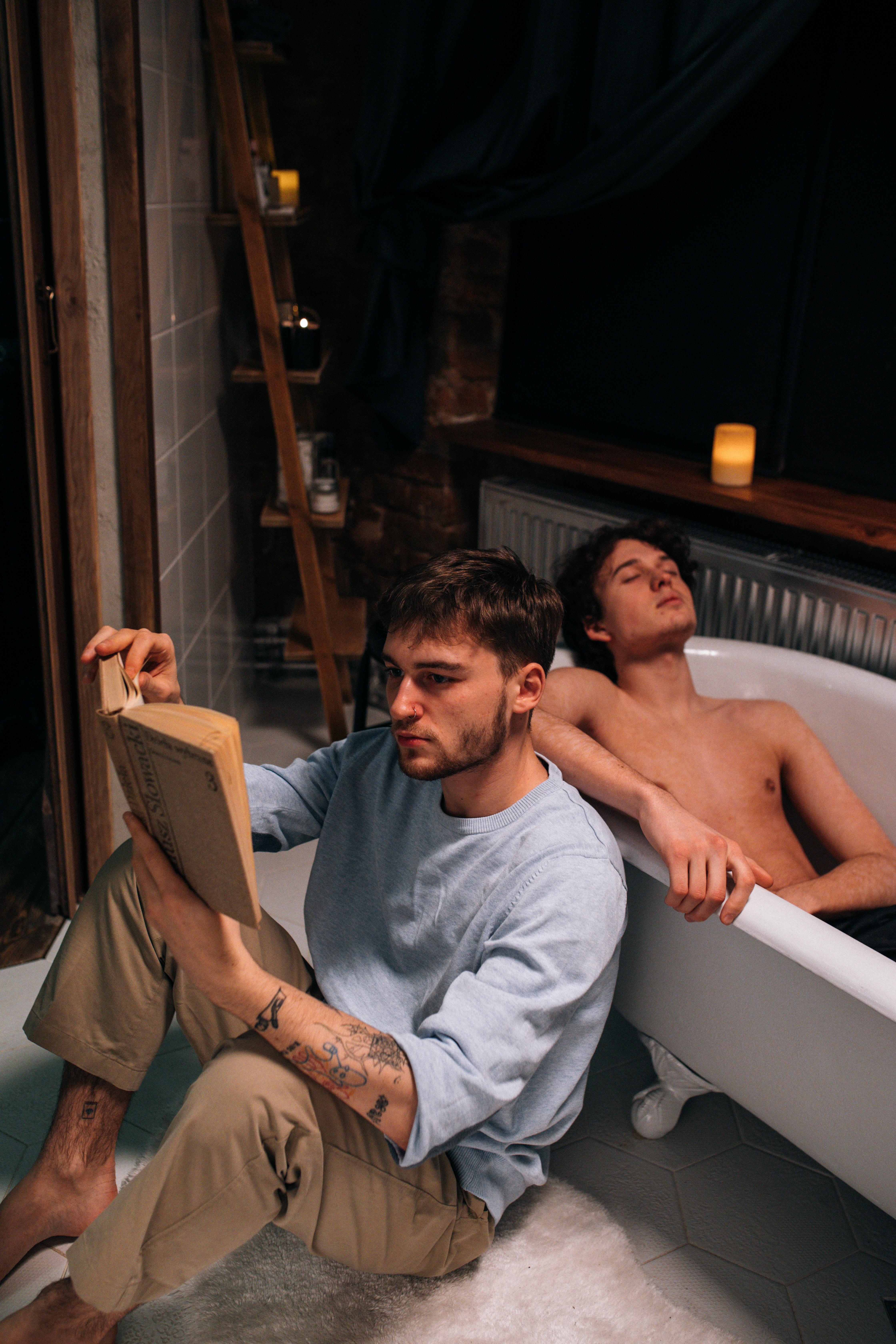 man in gray sweatshirt reading a book near a man taking a bath