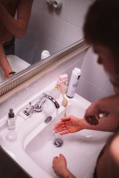 Top view of an adult washing hands in a clean, modern bathroom sink with running water.