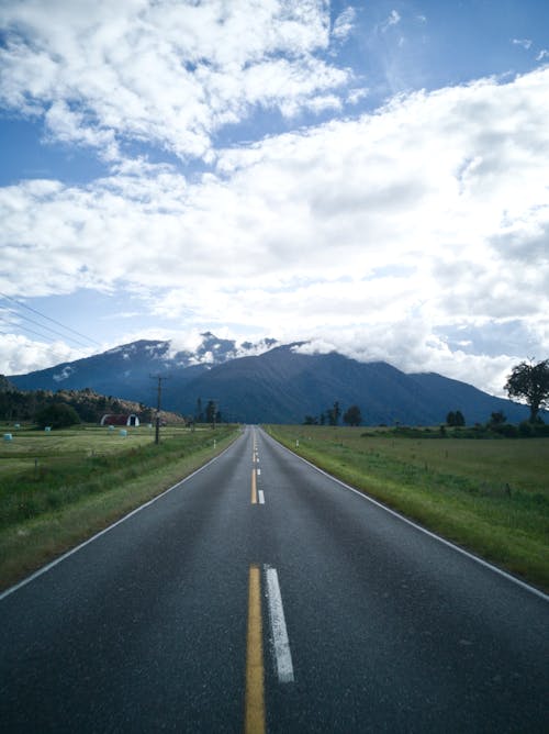 Empty Asphalt Road in Grass Field Leading to Mountains