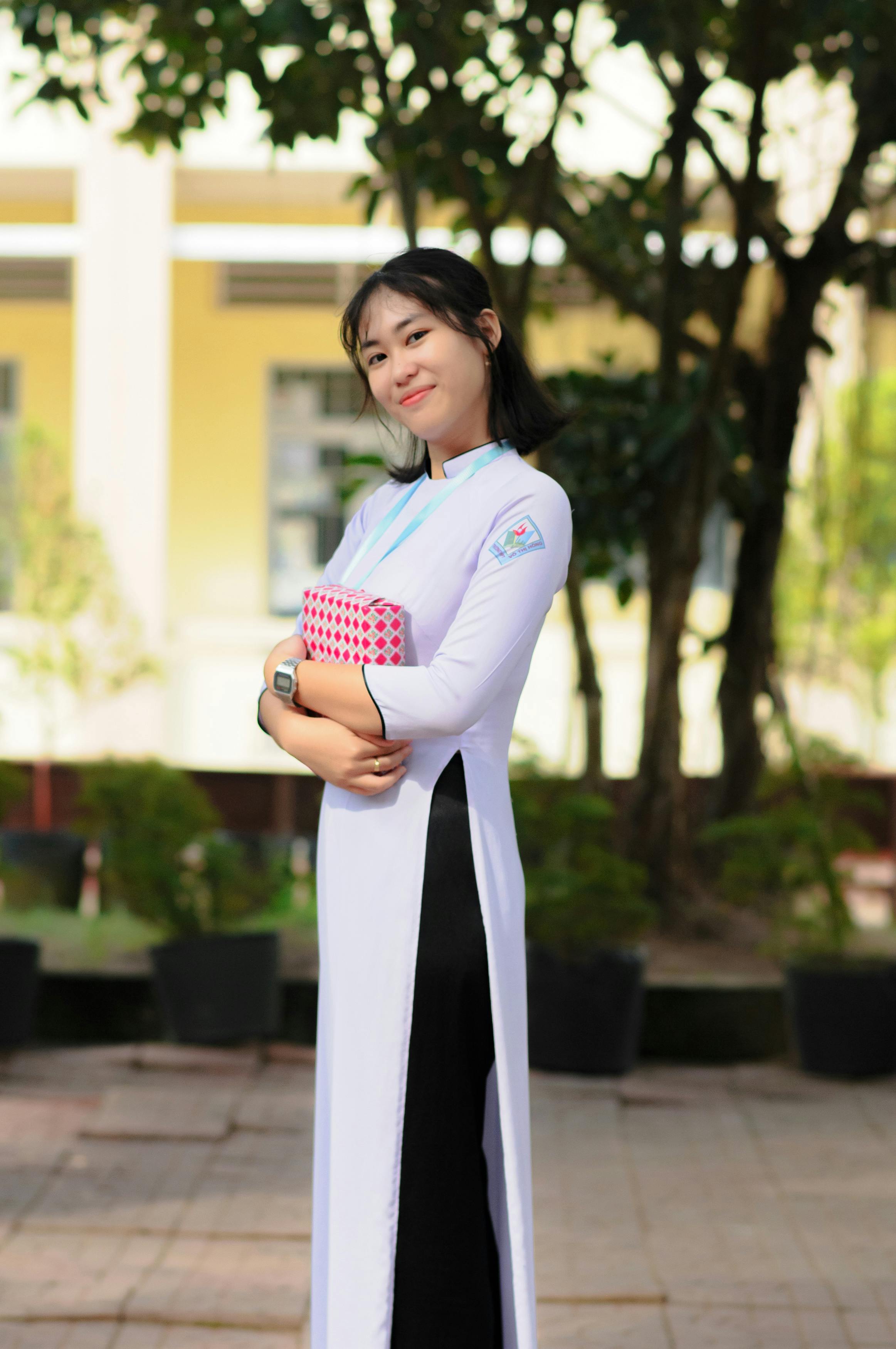 Smiling woman holding a gift in traditional Ao Dai outdoors.