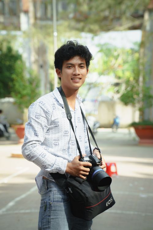 Free Young man holding a camera, smiling outdoors in daylight. Stock Photo