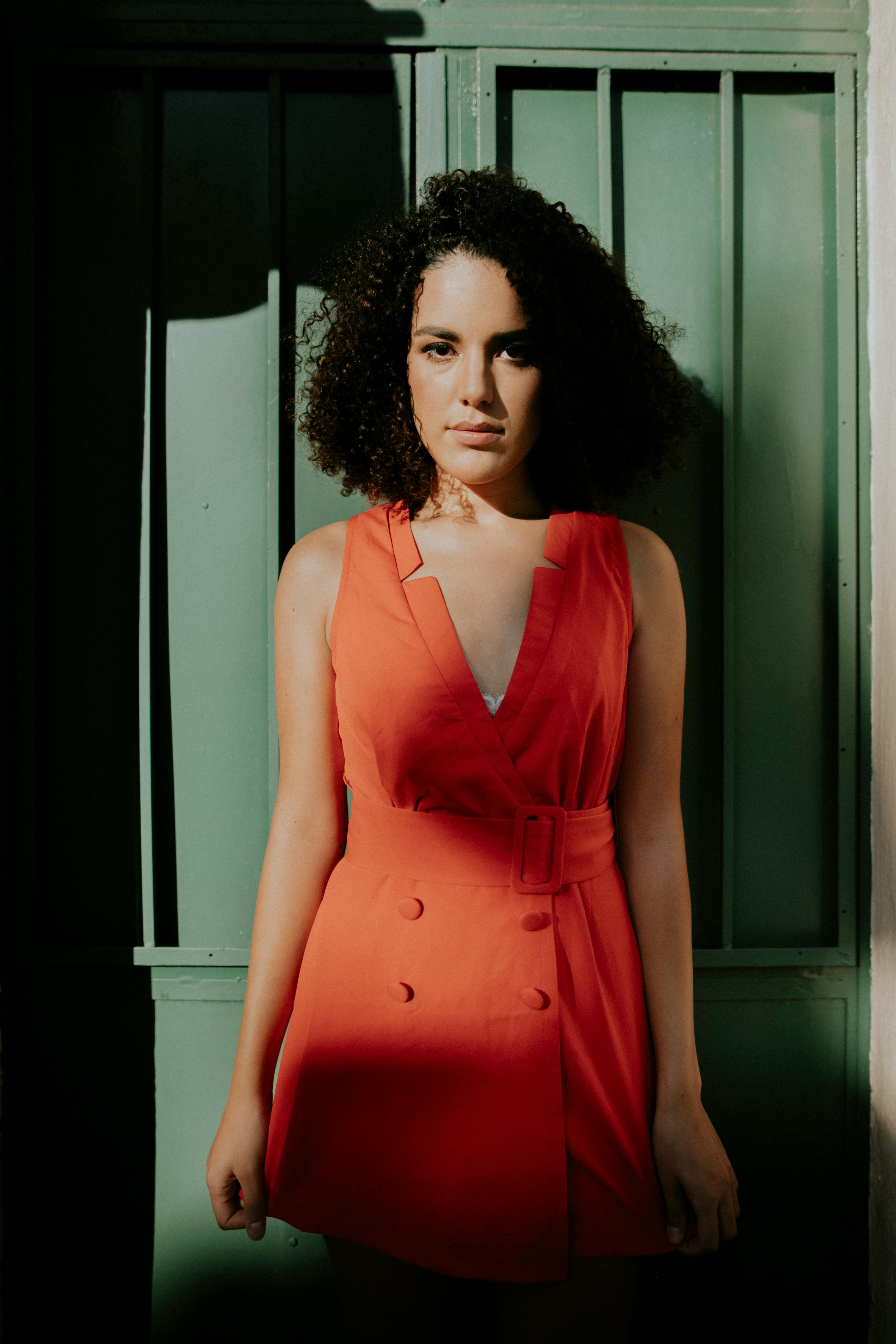 Elegant portrait of a woman wearing an orange dress posing against a green background, highlighting fashion and style.