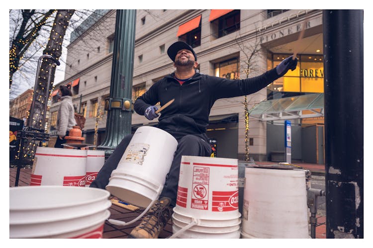 Happy Black Male Busker Playing Buckets On Street