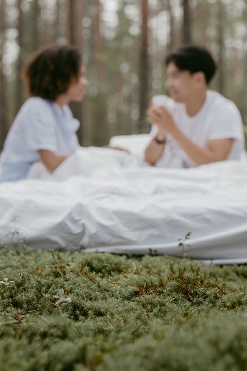 Free A couple enjoying a cozy morning with coffee amidst a serene forest landscape. Stock Photo