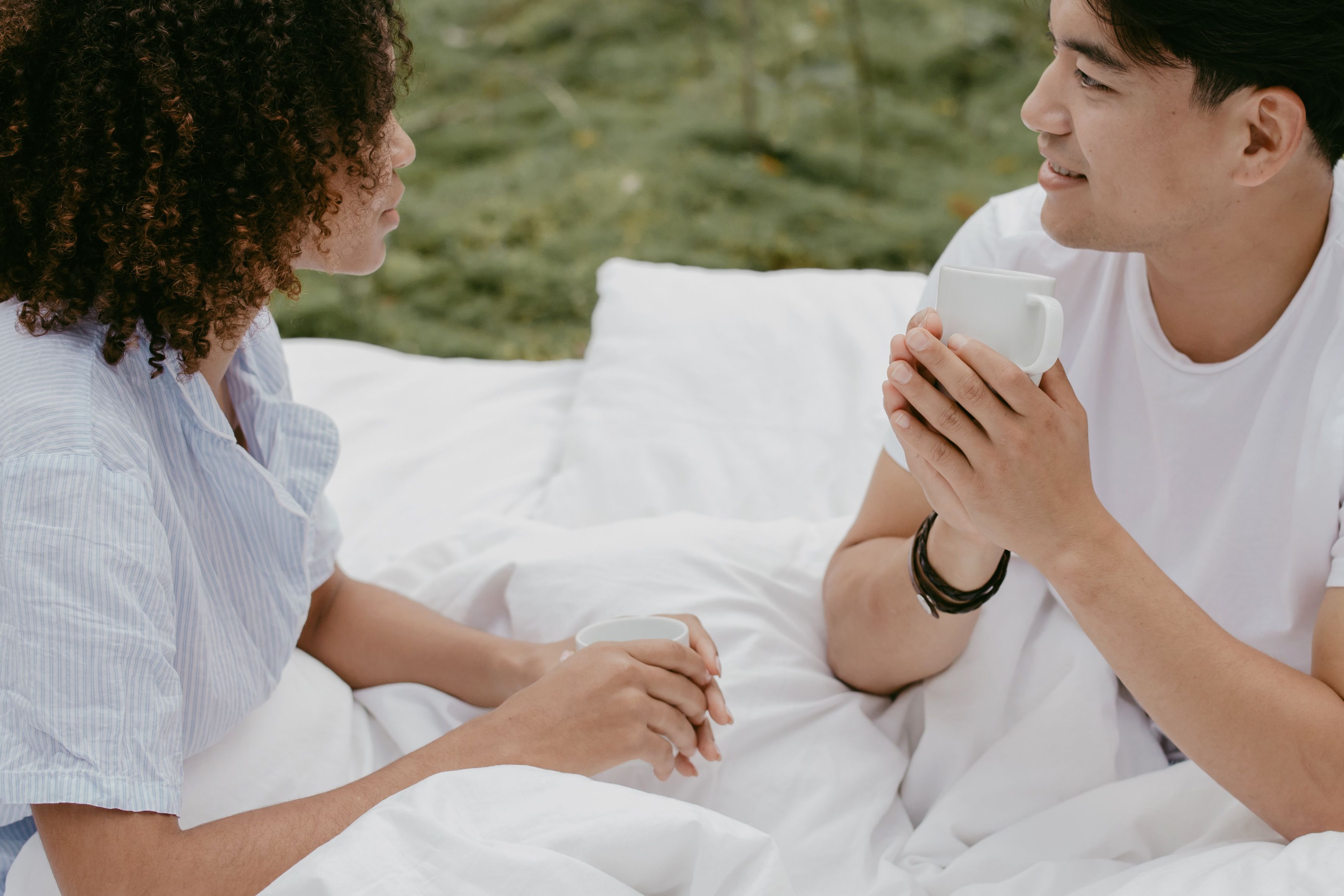 Couple sharing coffee outdoors on white bedding — unhurried presence