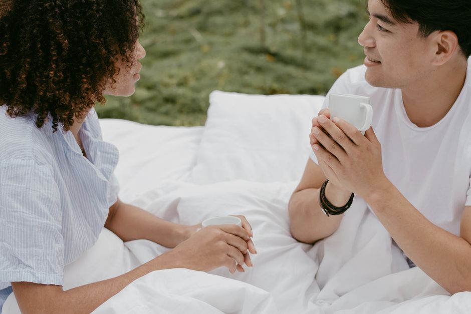 Couple sharing coffee outdoors on white bedding — unhurried presence