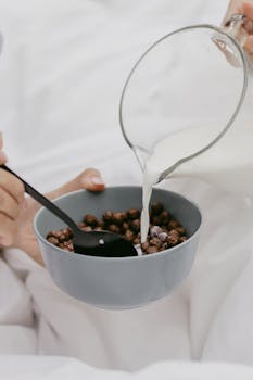 A close-up of chocolate cereal with milk being poured into a blue ceramic bowl.