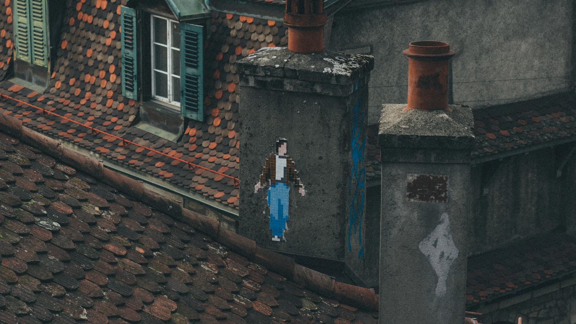 A rustic rooftop featuring unique pixel art graffiti on a chimney in an urban setting.