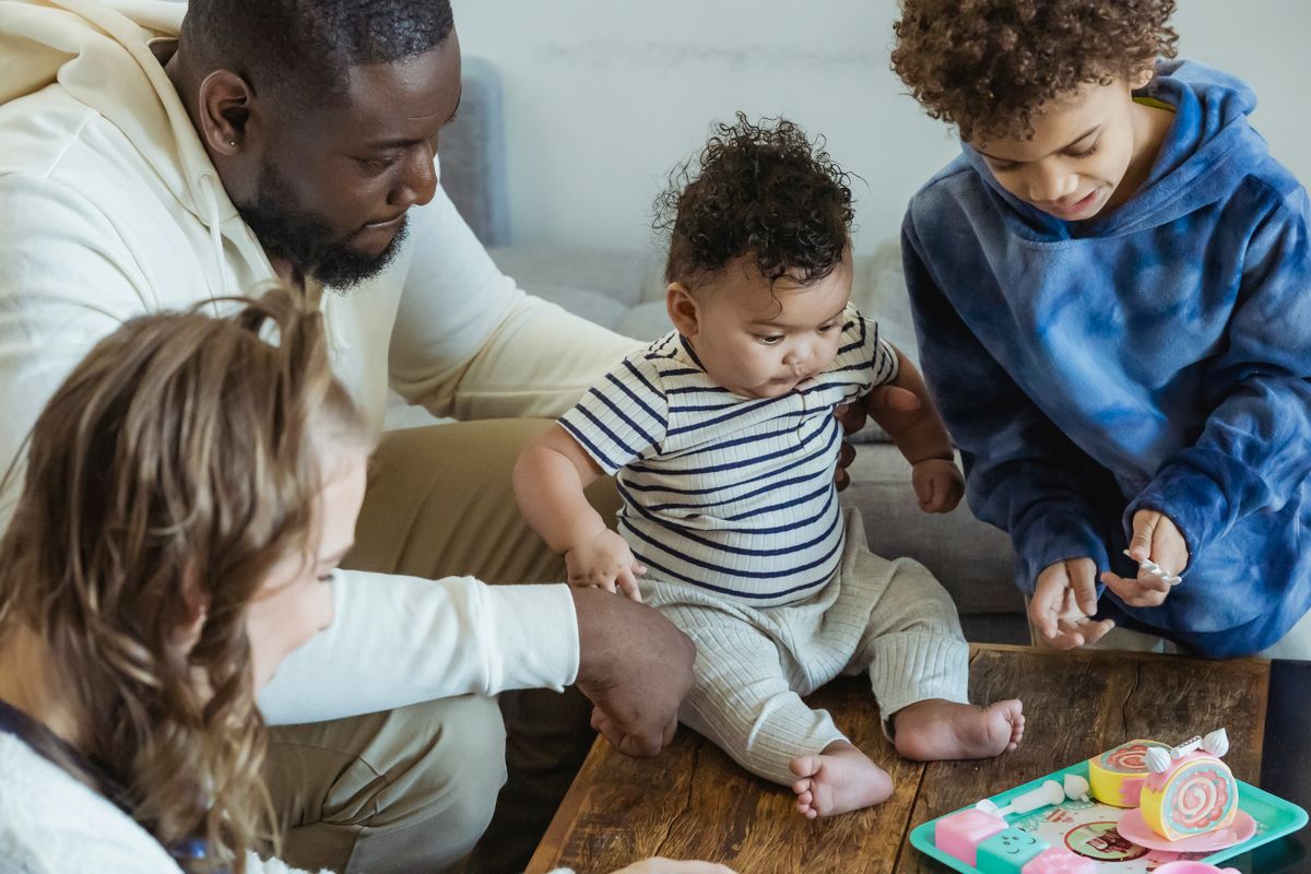 Família multirracial brincando com crianças em casa representando vínculo socioafetivo