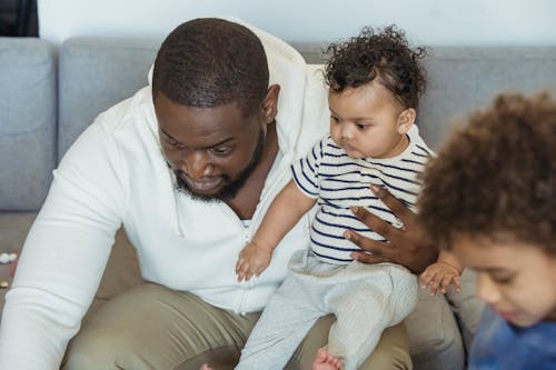 Free Bearded African American dad with cute little toddler in arms near crop son in lounge Stock Photo