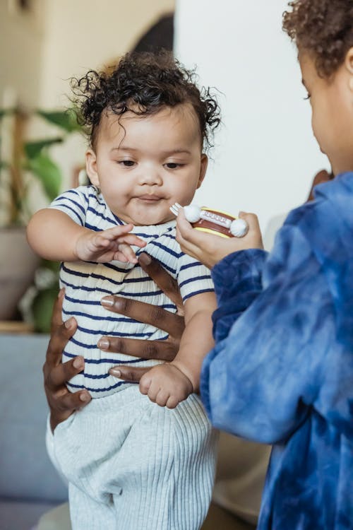 Black brother feeding little cute toddler held by parent