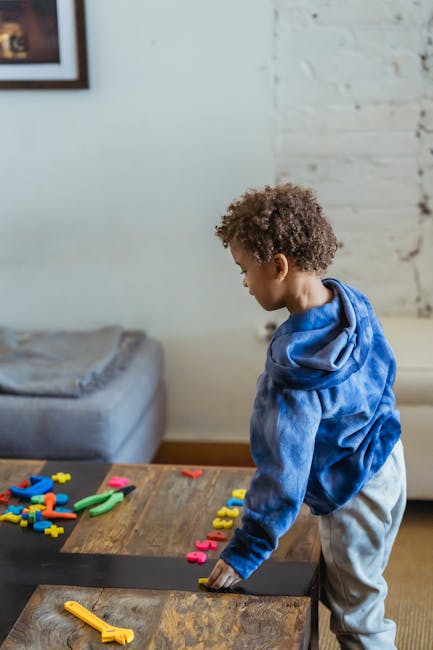 High angle side view of African American child placing toy numbers in row while standing at wooden table at home
