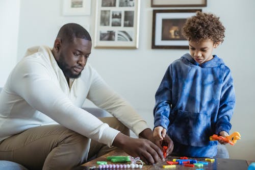 Serious African American father helping curly haired son during game with toy instruments at home