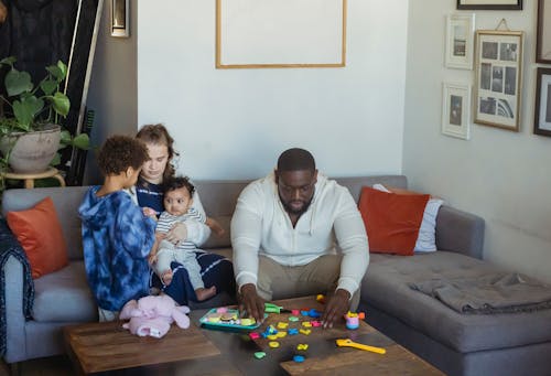 Free Black father playing toys sitting near wife cuddling baby and son while spending free time together at home Stock Photo