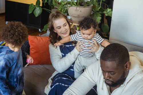 High angle of positive mother spending time with infant and son playing with toys near father