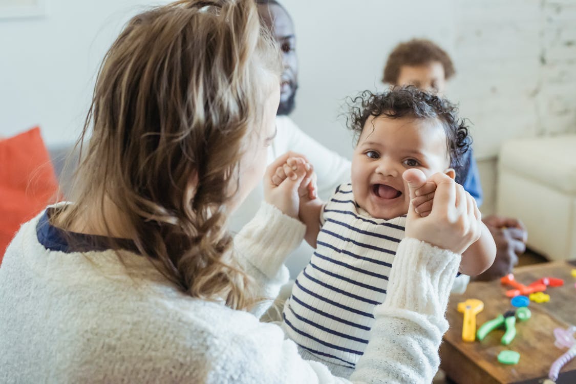 Free High angle of mum holding hands of small African American baby with mouth opened while sitting near father and son Stock Photo