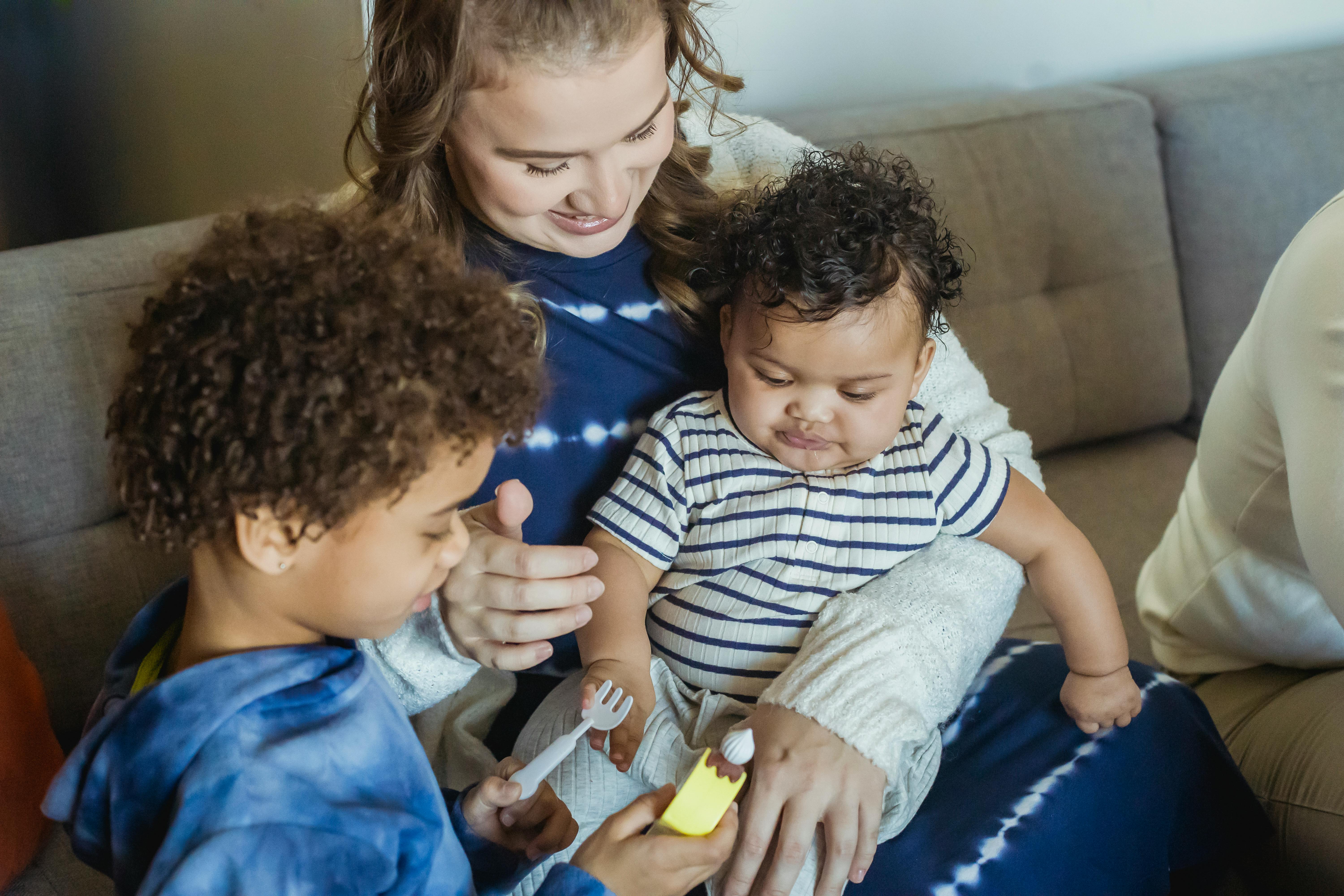 mother cuddling black baby and playing toys with son