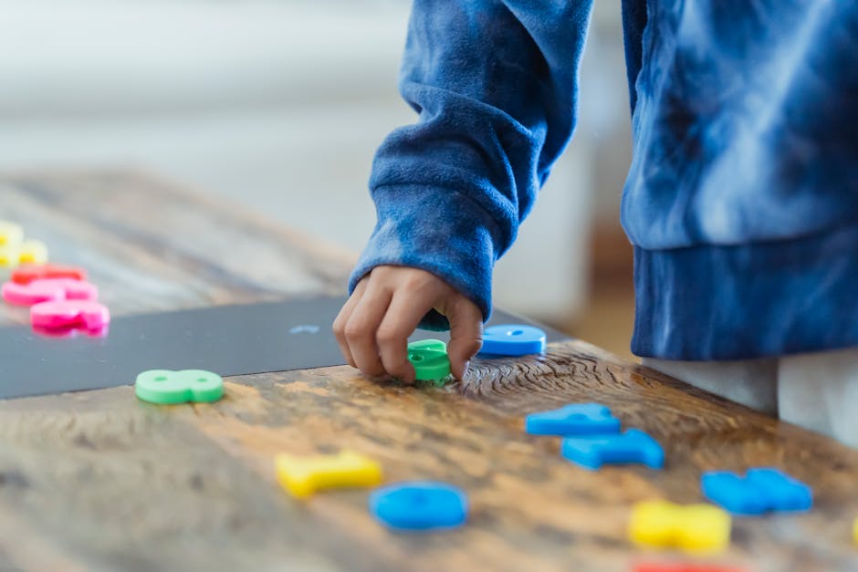 Crop anonymous ethnic boy taking plastic number from wooden table while learning math