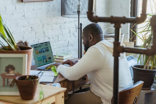 Free Side view of concentrated African American male freelancer sitting at wooden table and working online on netbook Stock Photo