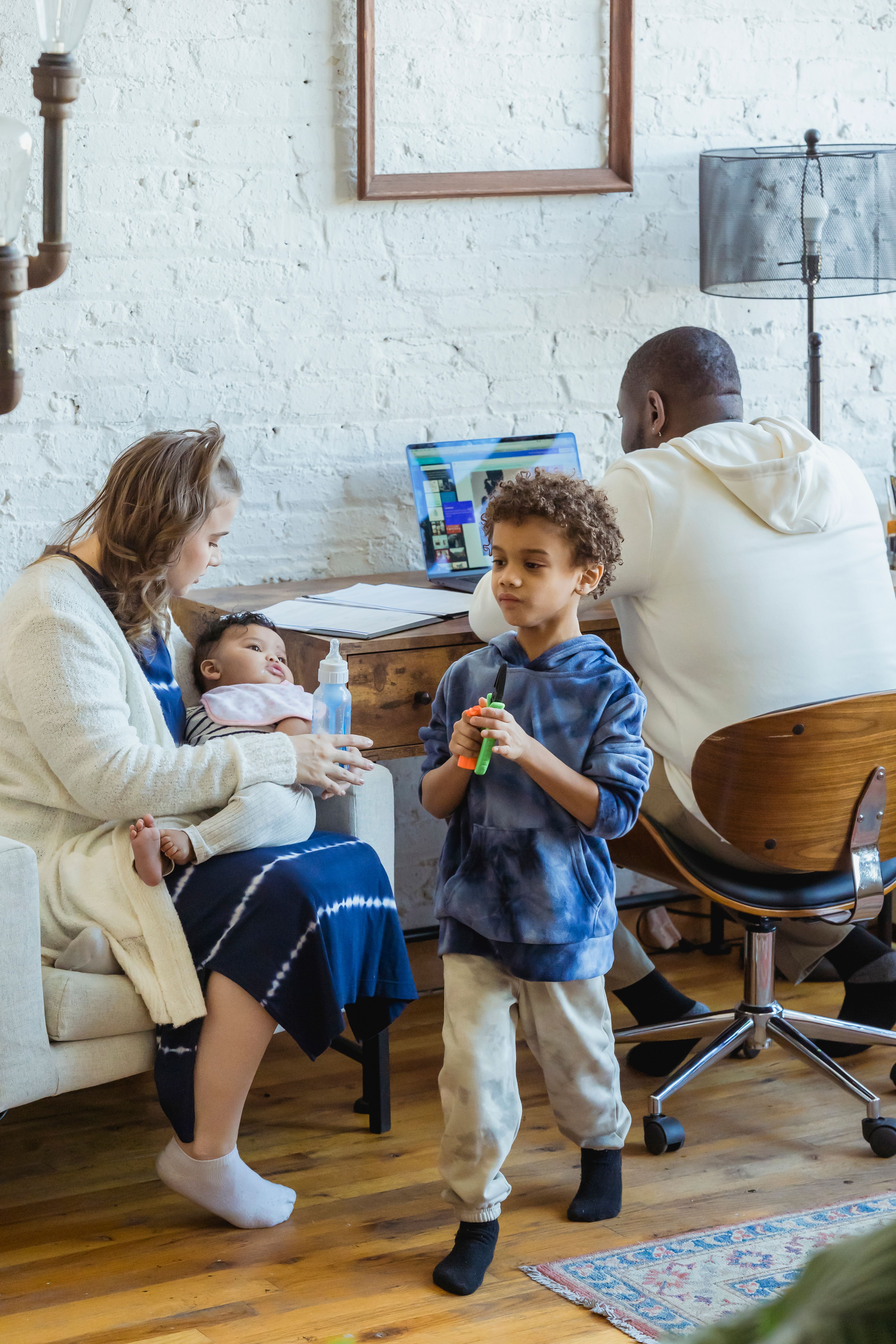 African American man working on netbook sitting at table near son playing toy and mother feeding baby from bottle