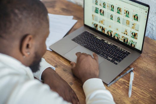A focused man browsing images on a laptop in a modern workspace setting.
