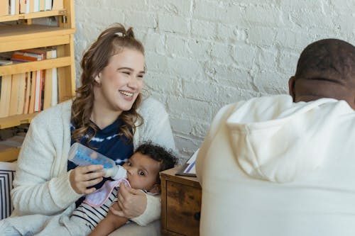 Free Cheerful mother feeding black baby sitting near busy father Stock Photo