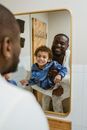 Cheerful African American father and son showing teeth and looking at reflection of mirror while doing morning routine in bathroom